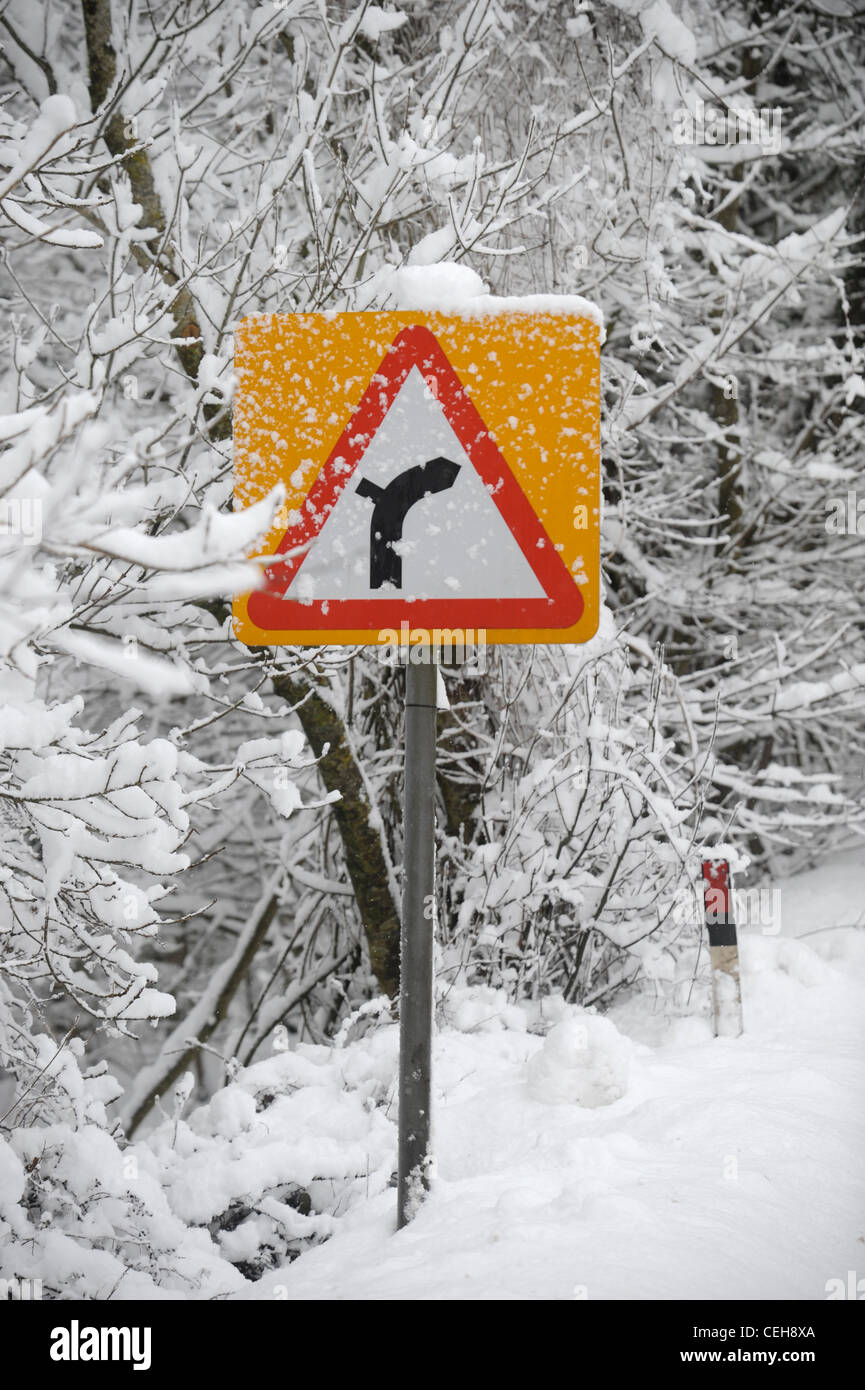 A traffic sign in snowy conditions warning of a bend in the road UK Stock Photo