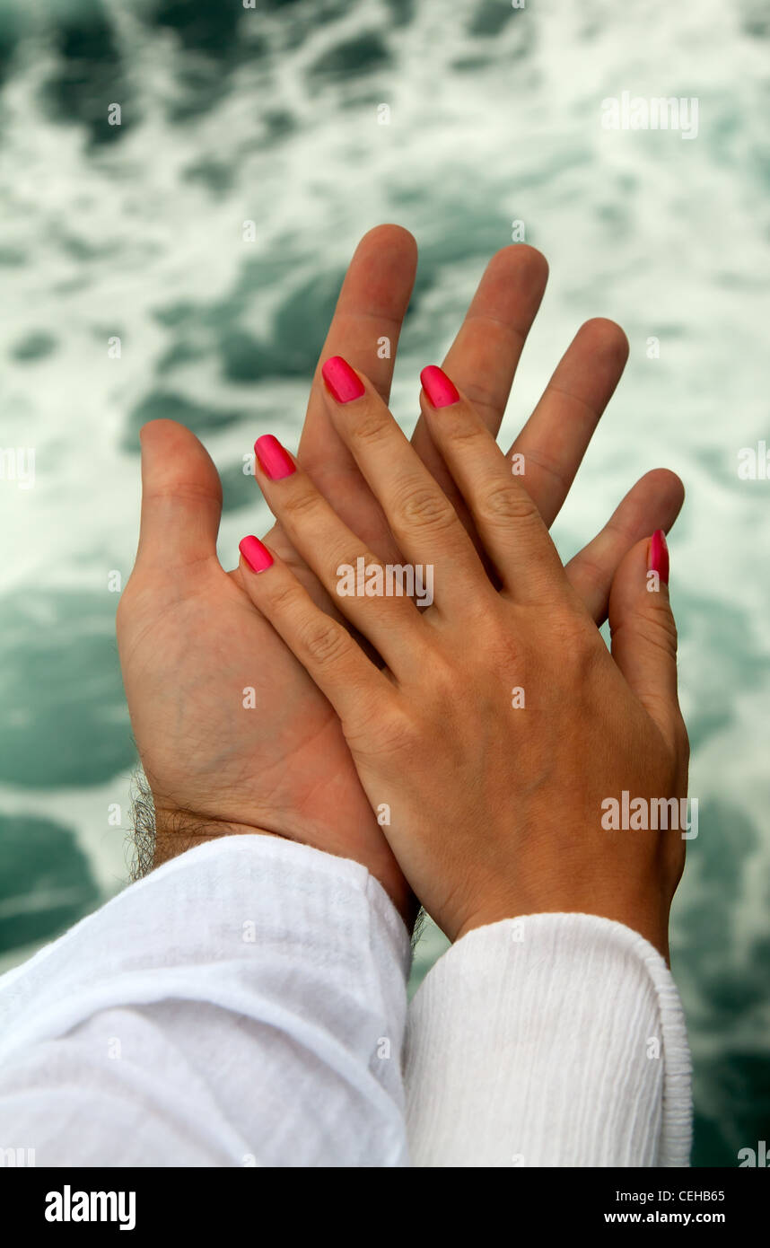 Men's and Women's tanned hands against the sea Stock Photo