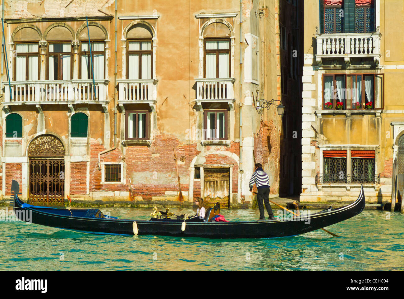 gondolier rowing a gondola with two tourists in it along a canal in front of a palazzo Venice italy ey europe Stock Photo