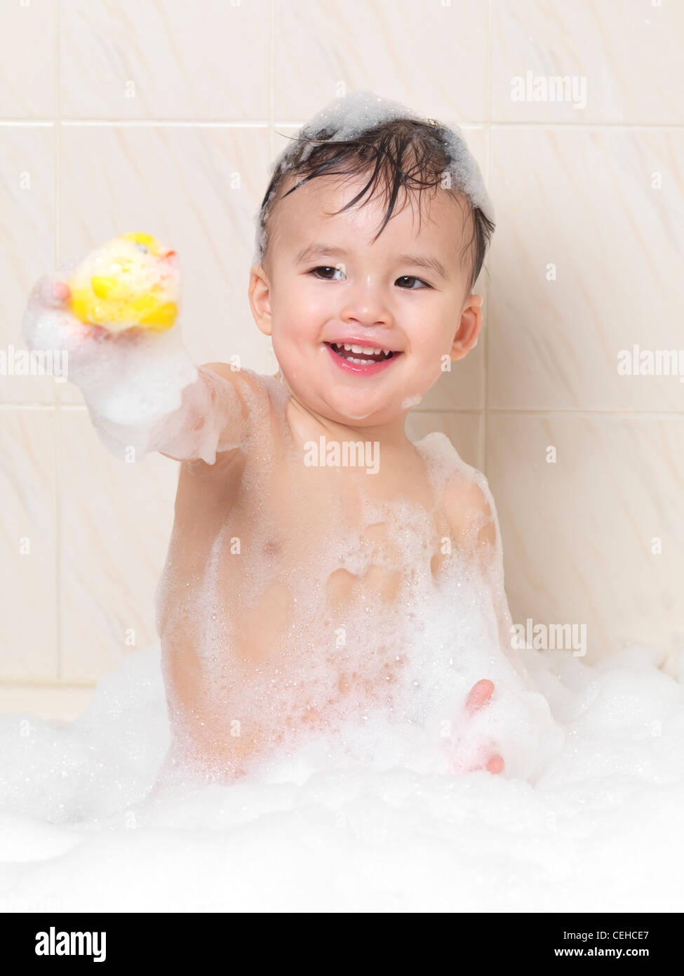 Two year old baby boy playing in a foam bath with a rubber duck Stock