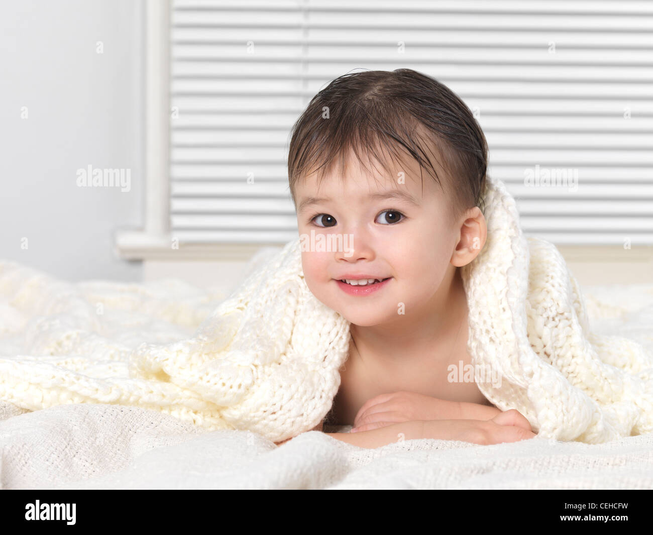 Cute smiling two year old baby boy peeking out from under a blanket