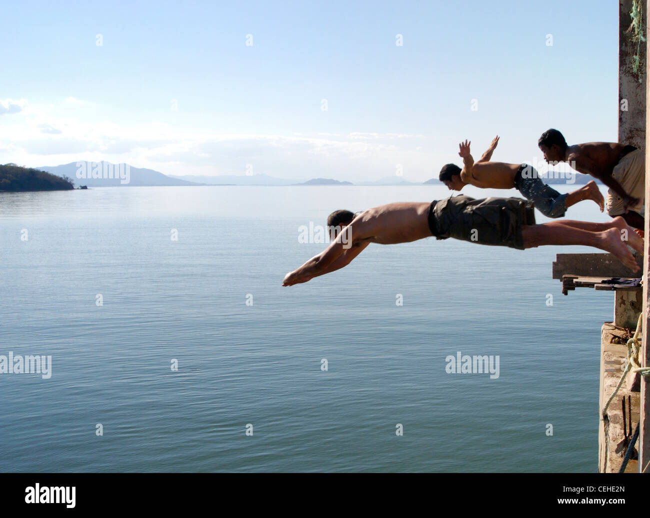 3 men make a coordinated dive with perfect timing into the tranquil waters of San Lucas lake, Costa Rica Stock Photo
