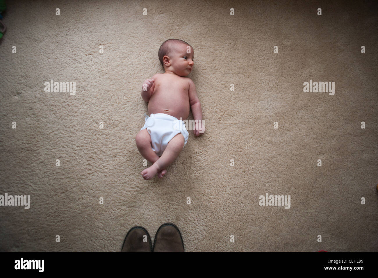 A newborn baby girl laying on the floor in front of the tips of shoes, showing the small size of the infant. Stock Photo