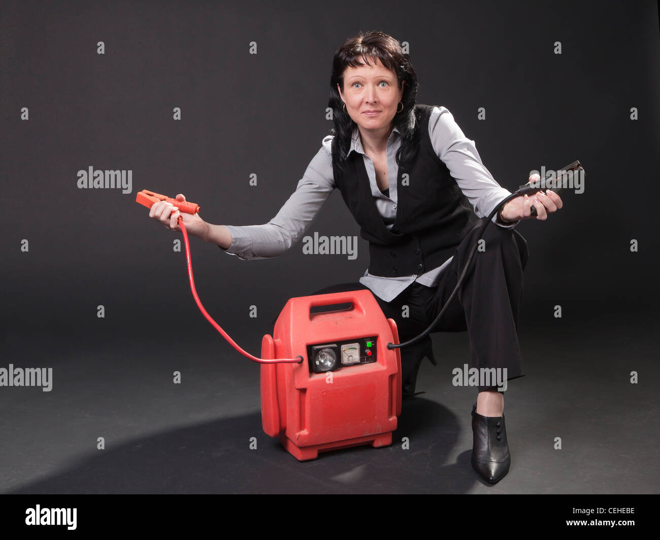 The adult middle-aged woman who is a car seller is in studio with battery booster power starter with start-up cables. Stock Photo