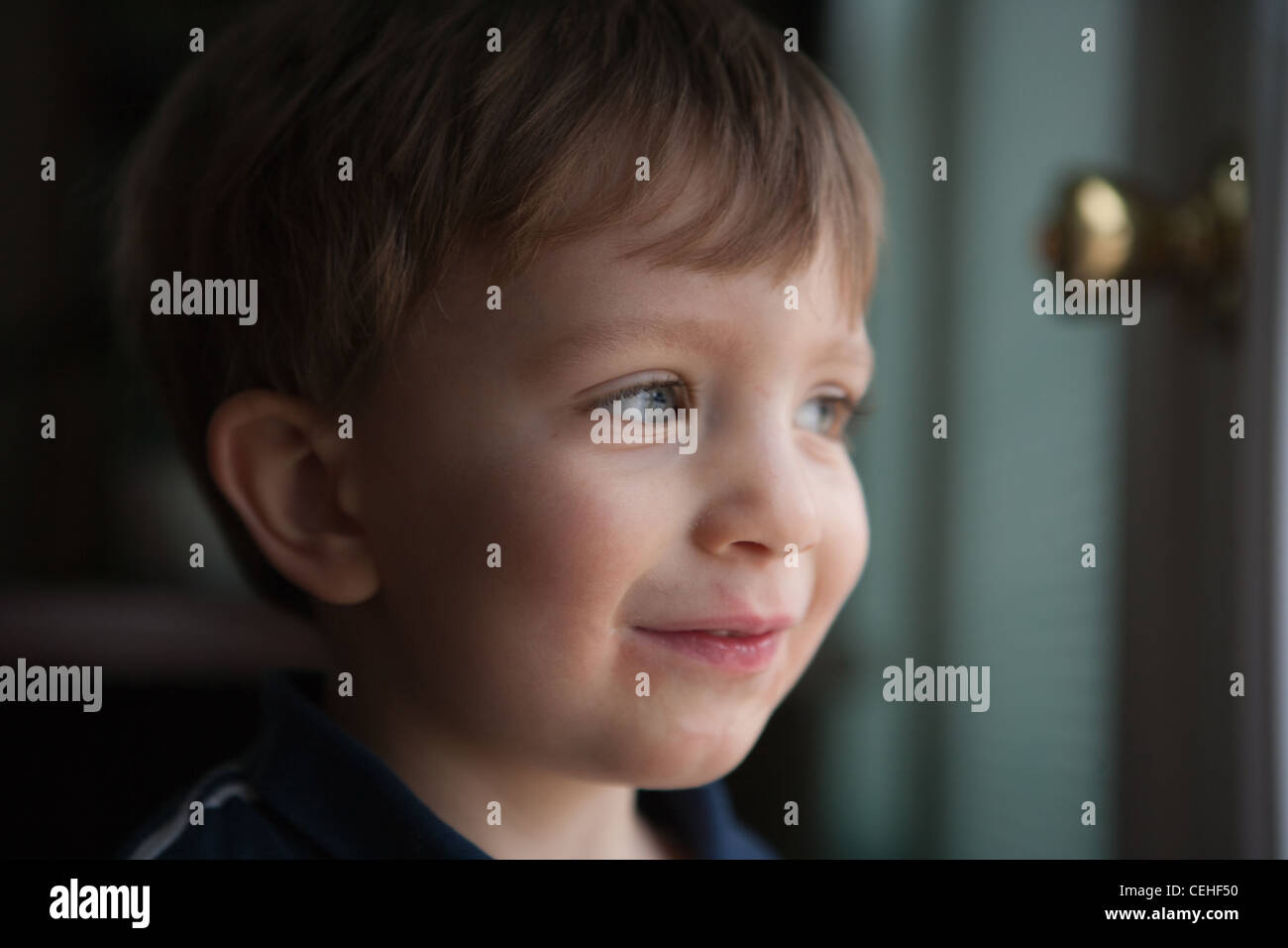 Two year old boy looking out the window, looking mischevious, smiling. Stock Photo