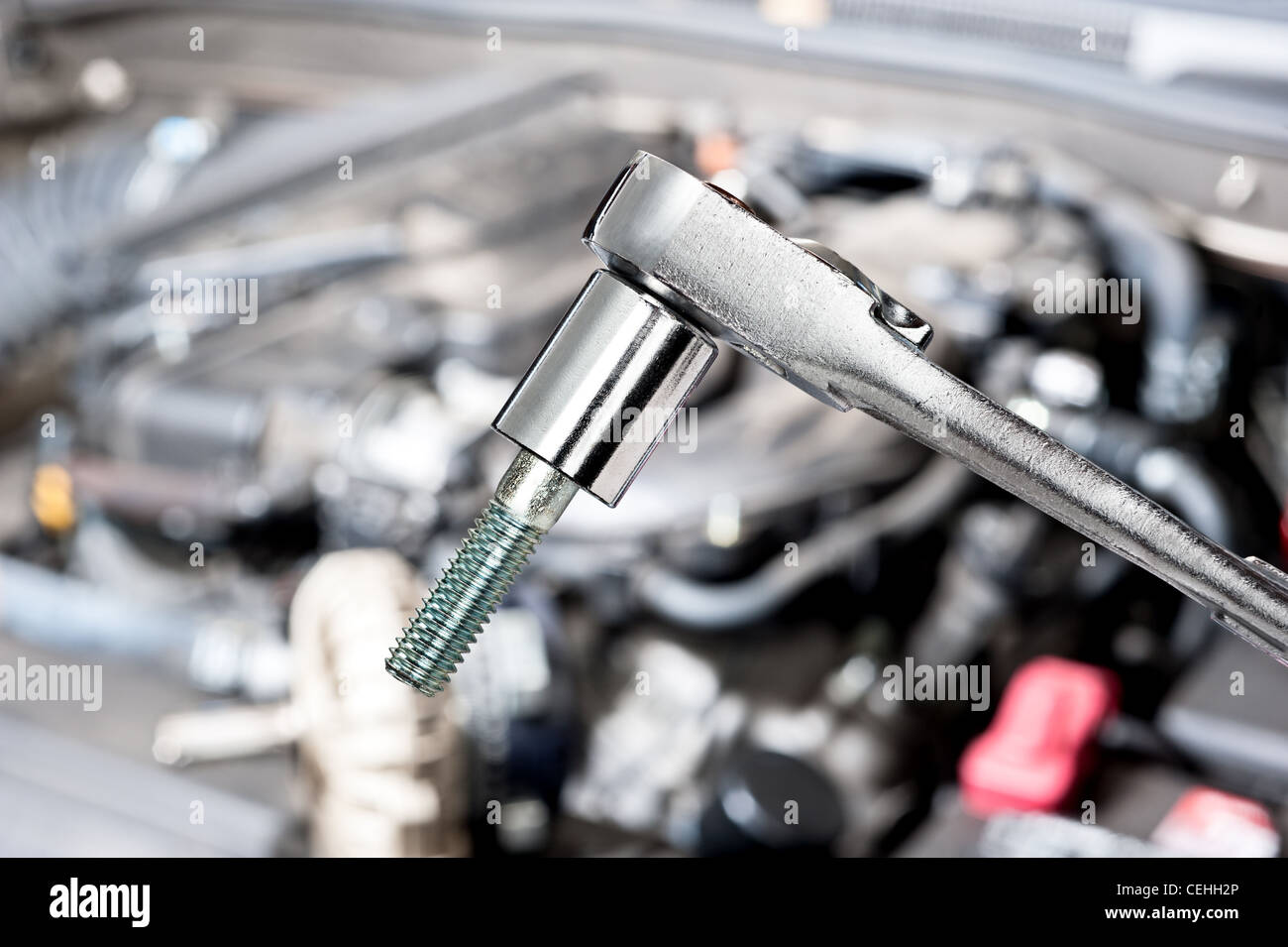 A shiny chrome socket wrench in front of a car engine before for servicing and repair Stock Photo