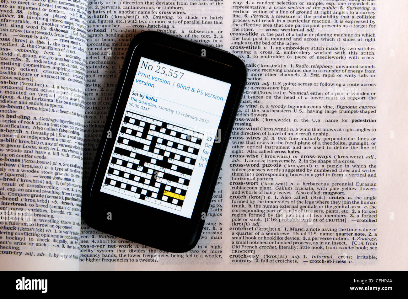 An online crossword puzzle displayed on a smartphone laying on a dictionary showing the definition of crossword puzzle. Stock Photo