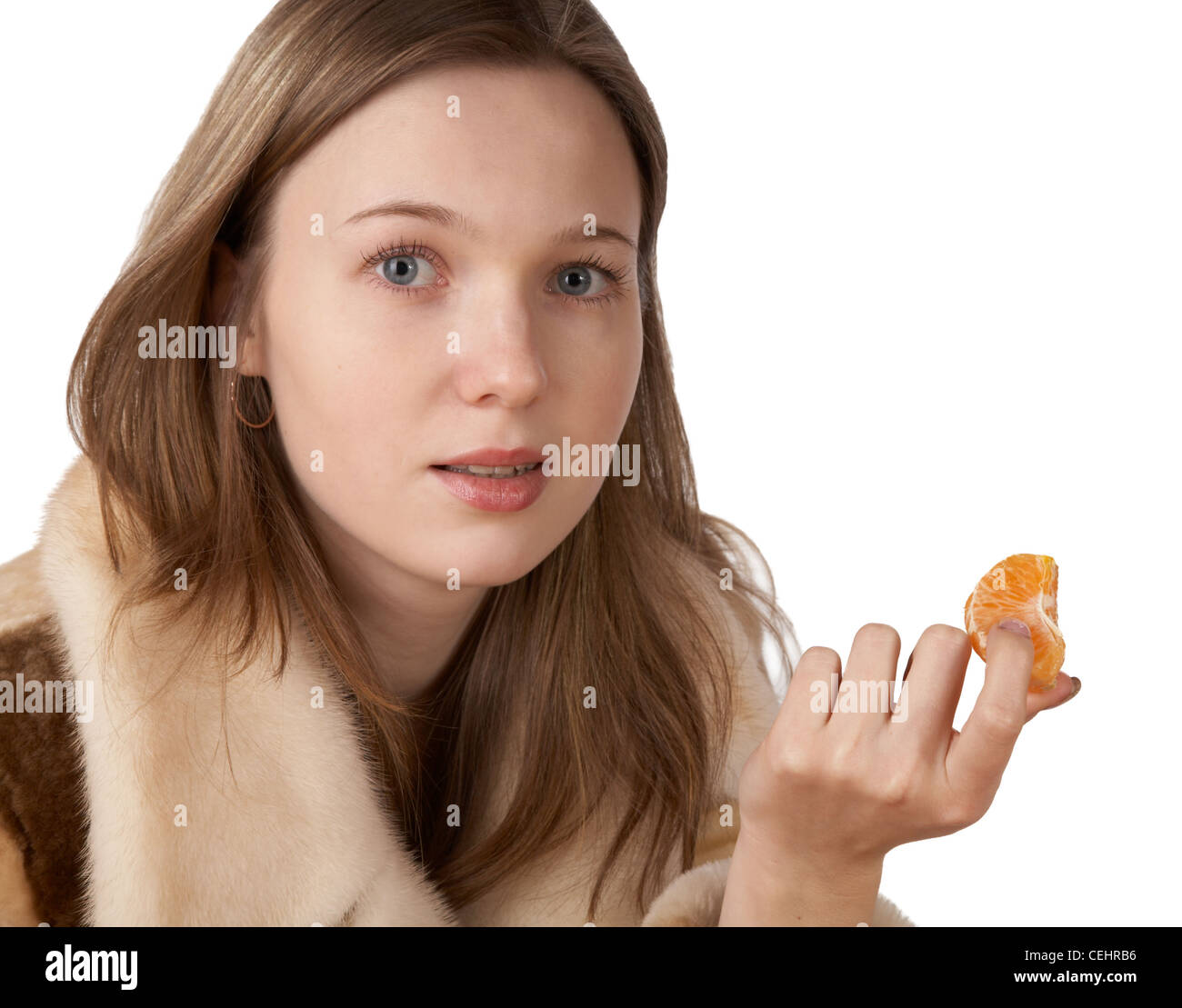 The girl in a fur coat holds segment of tangerine on white background