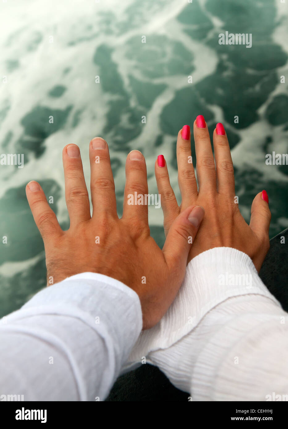 Men's and Women's tanned hands against the raging sea Stock Photo