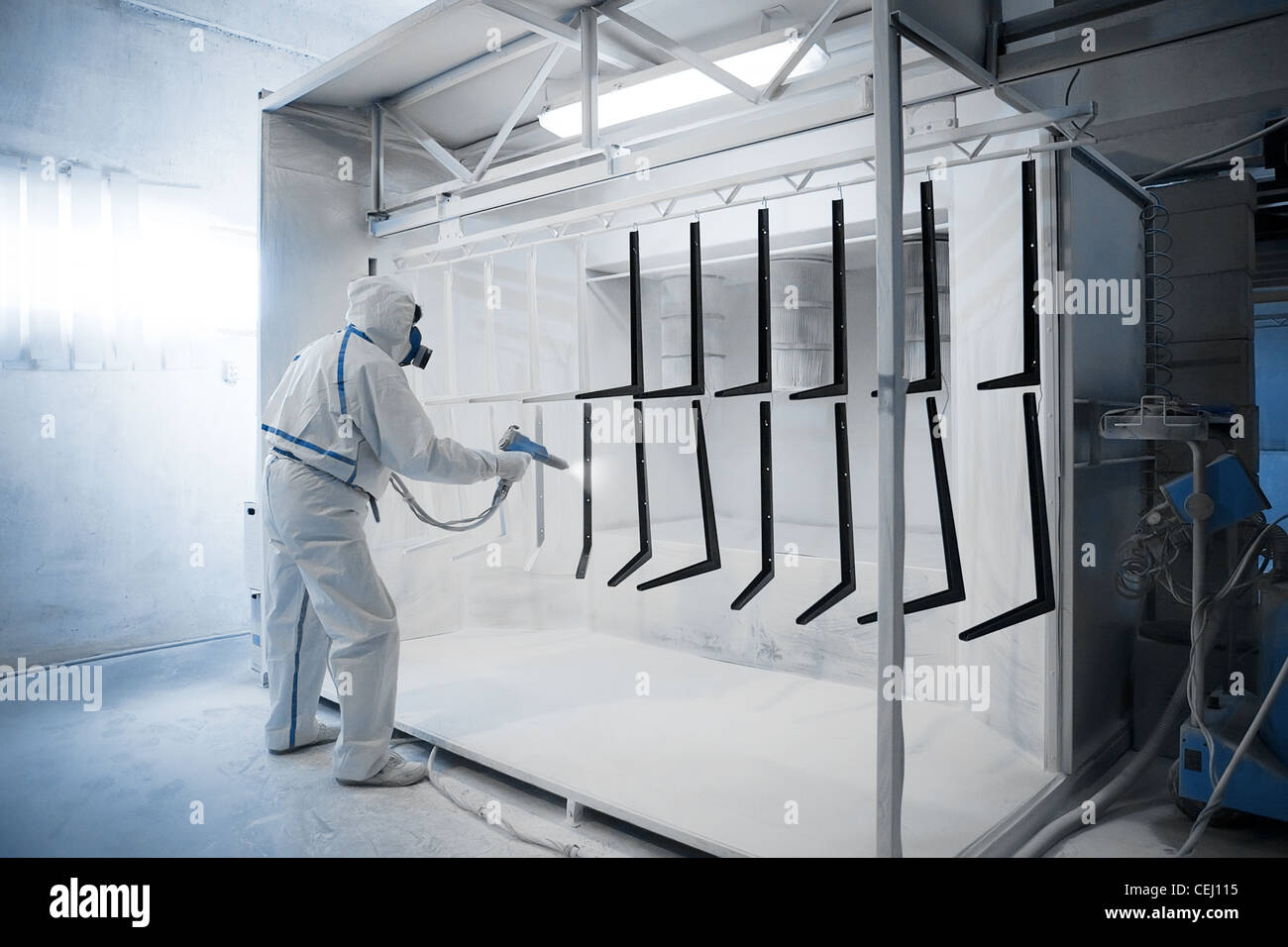 Worker wearing protective wear performing powder coating of metal