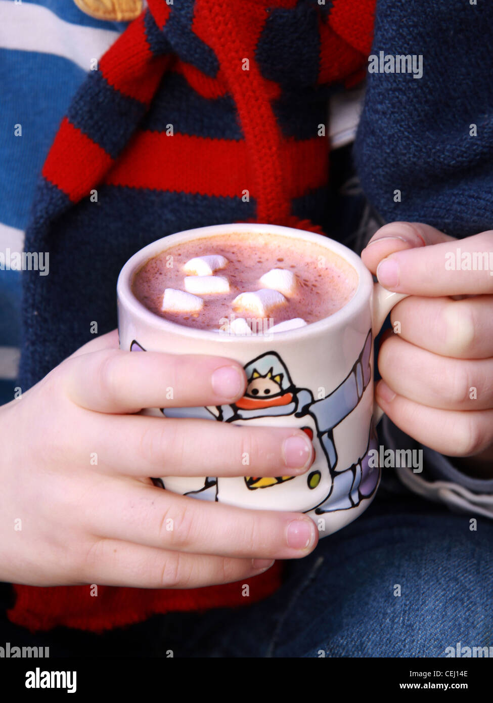 childs hands cradle warm mug of hot chocolate with marsh mallows Stock Photo