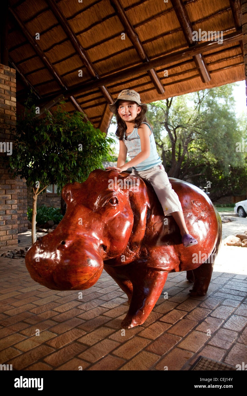 Little girl sitting on hippo sculpture at entrance to Bakubang Safari Lodge,Pilanesberg Game Reserve,North West Province Stock Photo