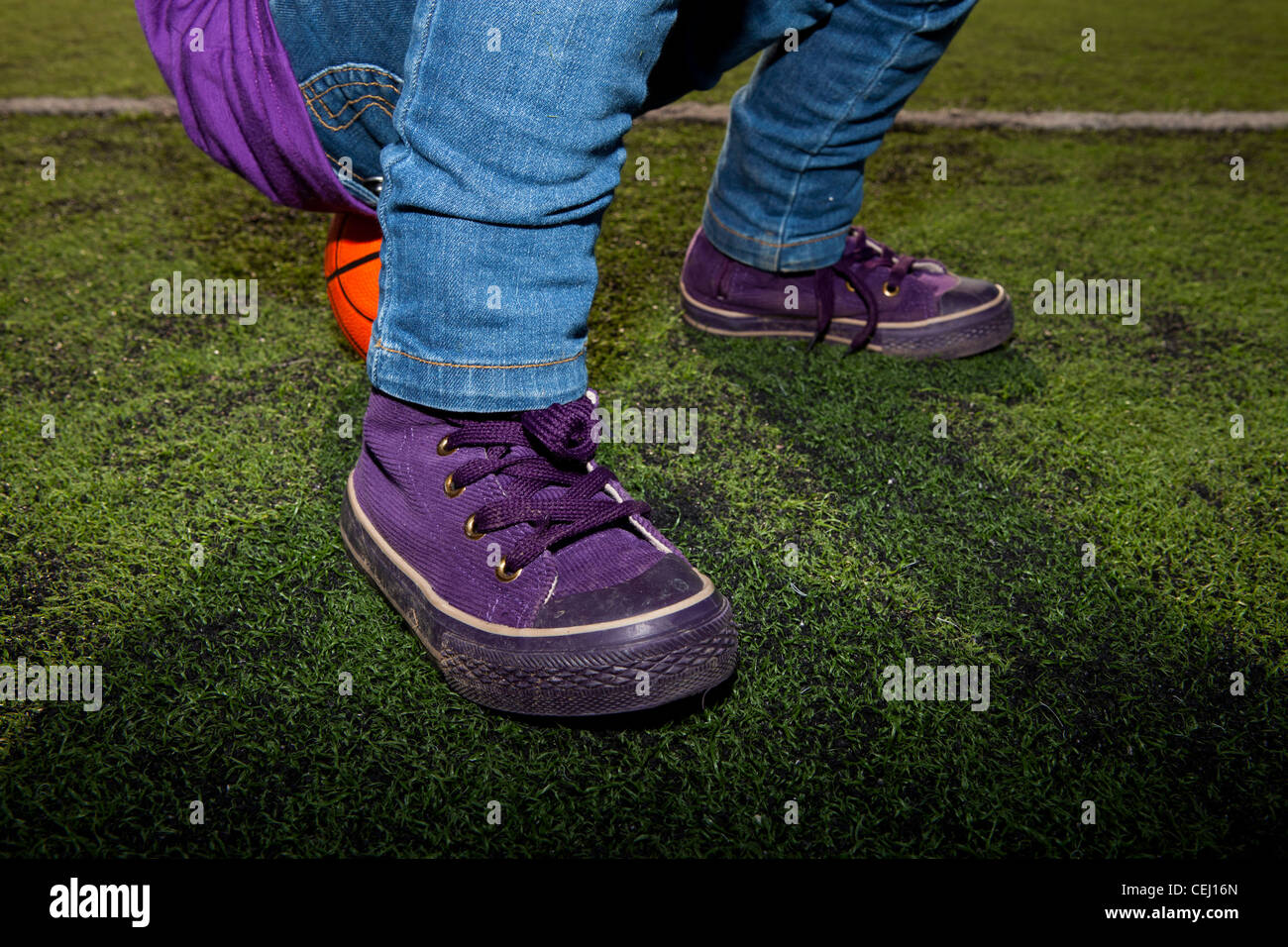 Closeup of a child sitting on a basketball with jeans and sneakers on