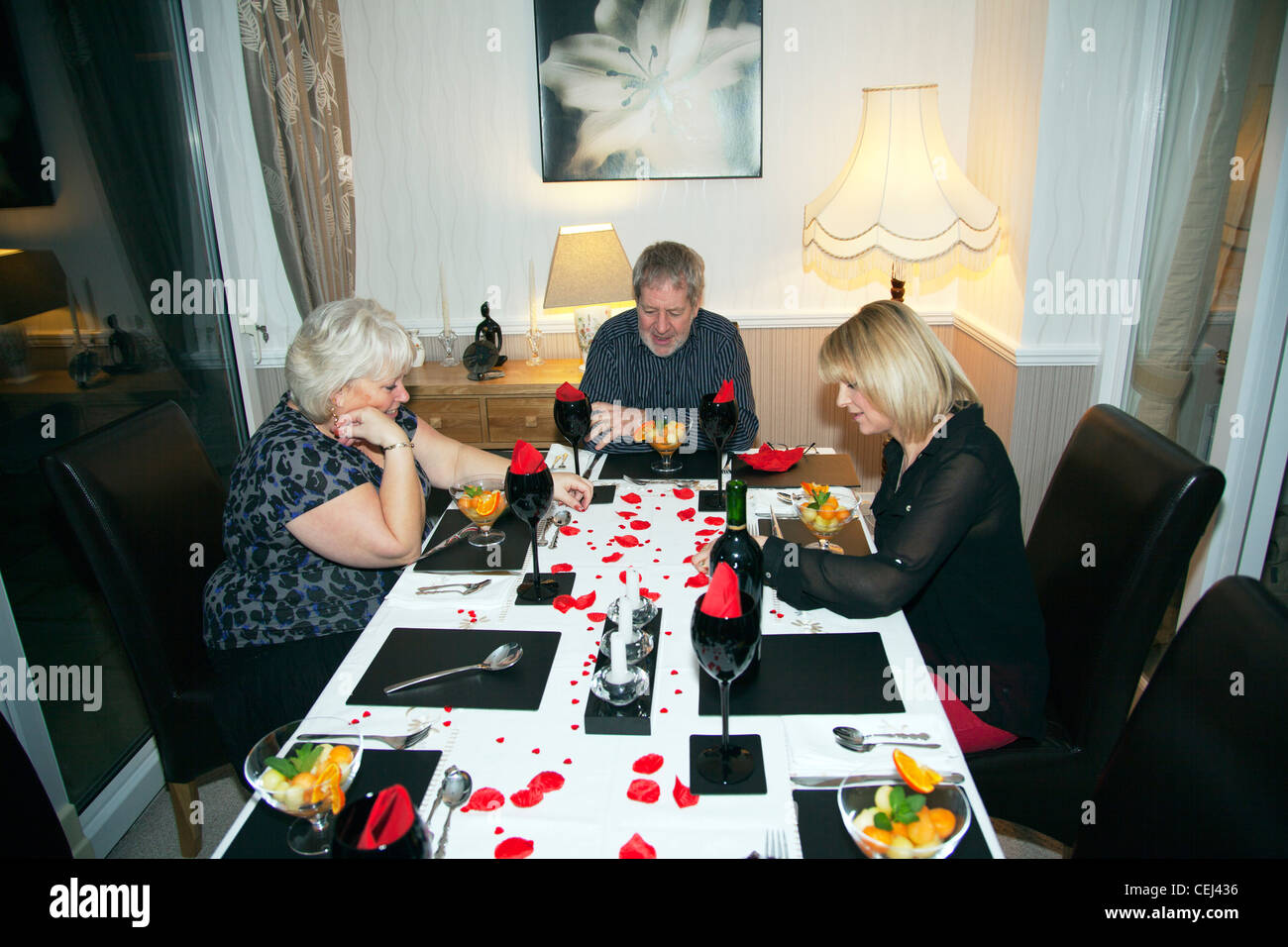 Three people sat at dinner table waiting for food to be served at home