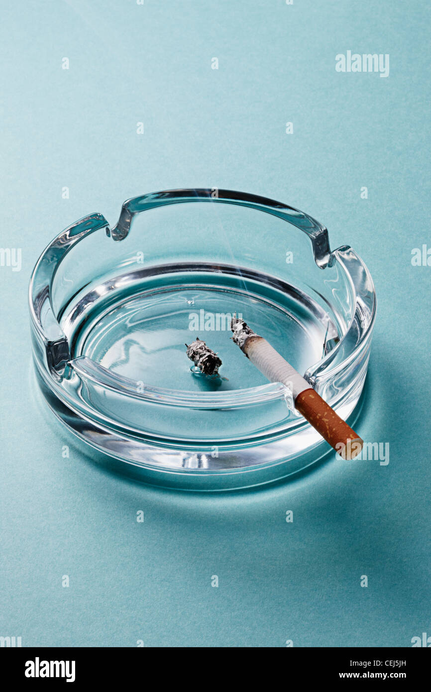 cigarette burning in a glass ashtray Stock Photo
