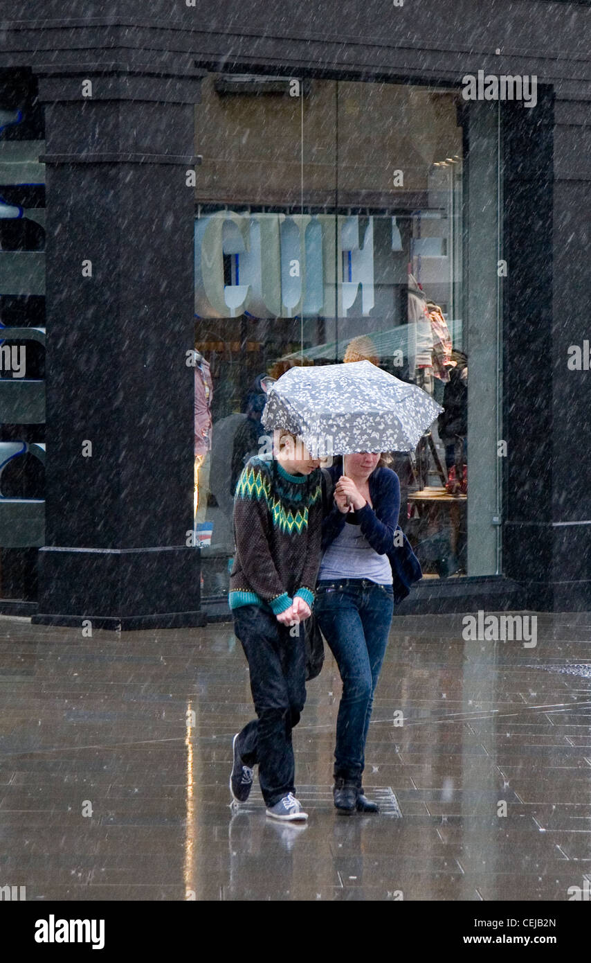 Two young people share a small umbrella during a heavy rainstorm Stock Photo