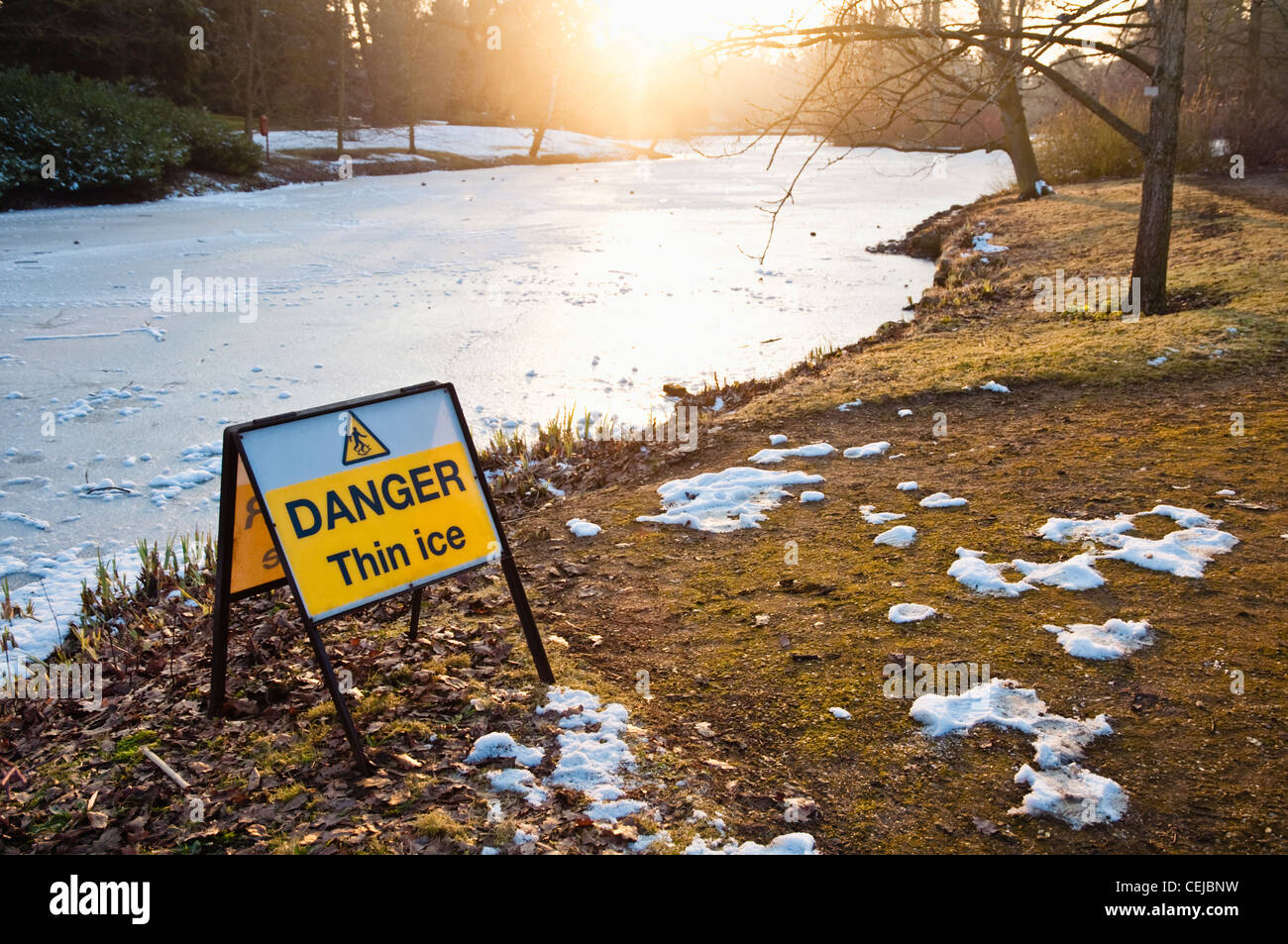 'Danger Thin Ice' sign beside a frozen lake lit up with winter sunshine. UK Stock Photo