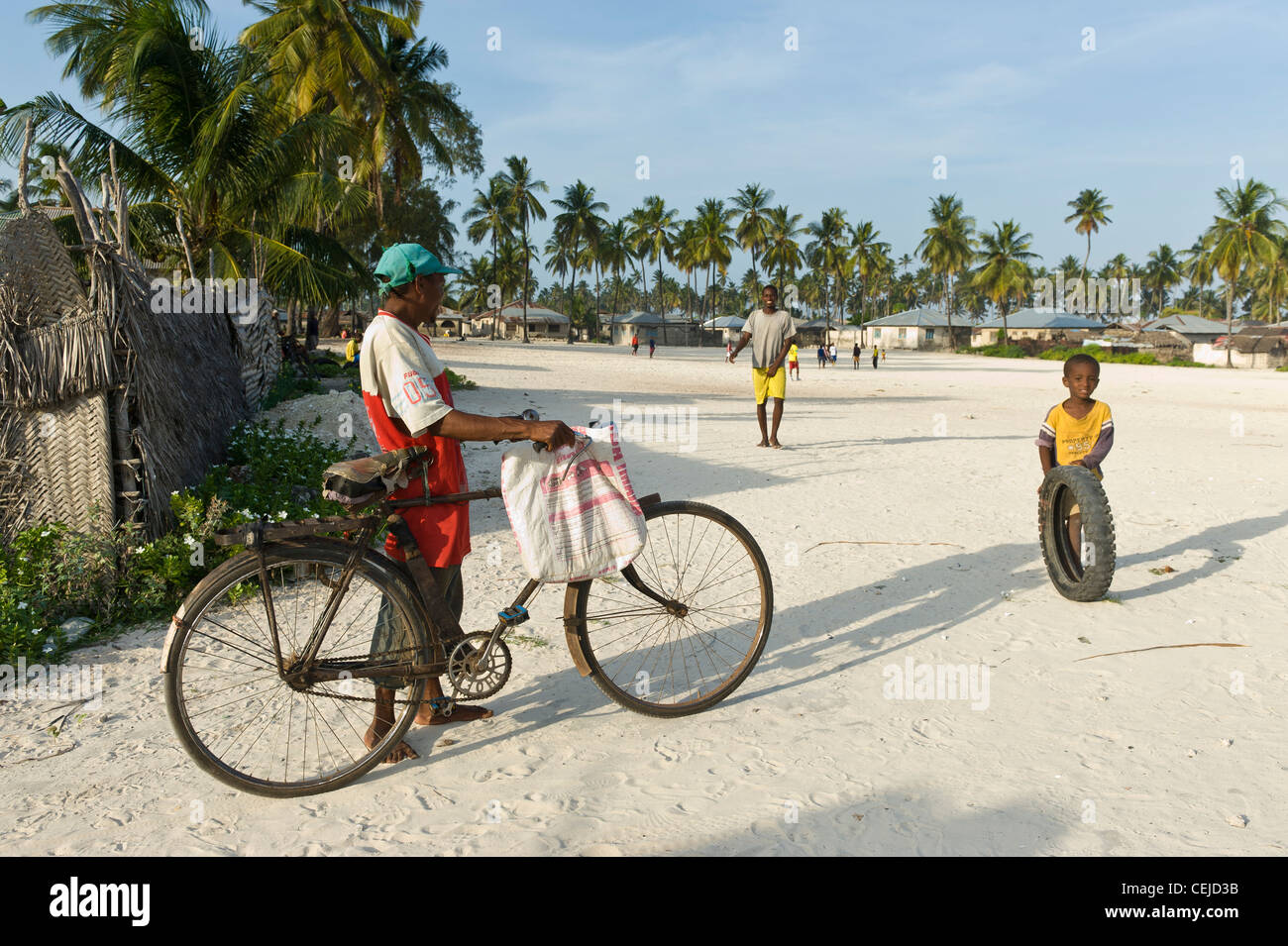 Man with a bicycle talking to a boy playing with a tire Bwejuu village east coast of Zanzibar Tanzania Stock Photo