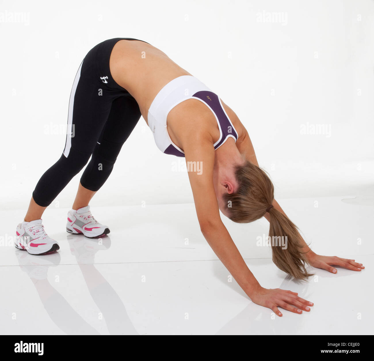 Upper body exercise Female fair hair tied into ponytail, wearing a cropped vest, black leggings and trainers, bending over Stock Photo