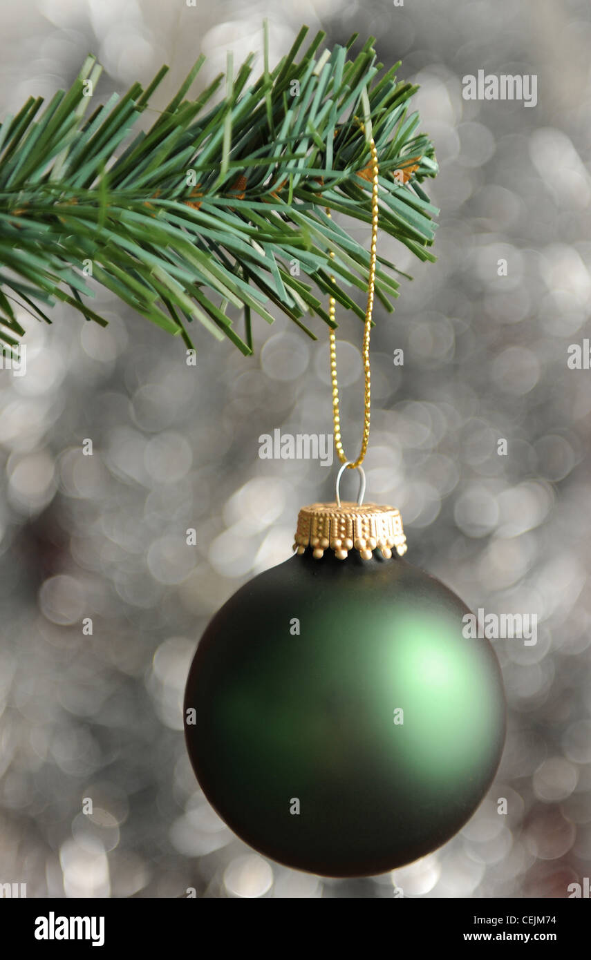 A green and metallic gold bauble hanging off the branch of a christmas tree, with a sparkly metallic silver background Stock Photo