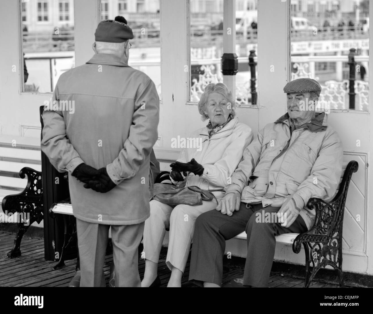 Black and white image of elderly friends sitting and talking to each other on a cold day in Winter in England, UK. Stock Photo