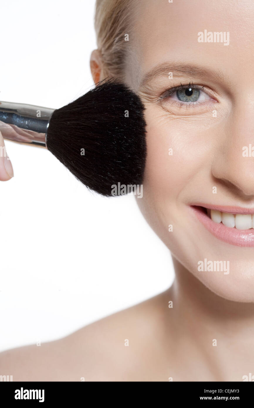 Female wearing subtle make up, applying blusher to her cheek, smiling, looking at camera Stock Photo