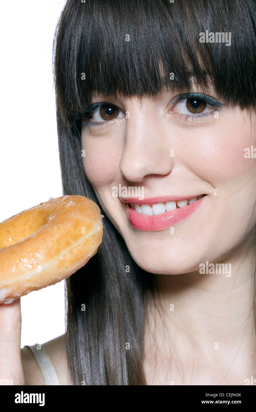 Female long fringed brunette hair, wearing green metallic eyeshadow and pink lipgloss, eating doughnut, smiling, looking at Stock Photo