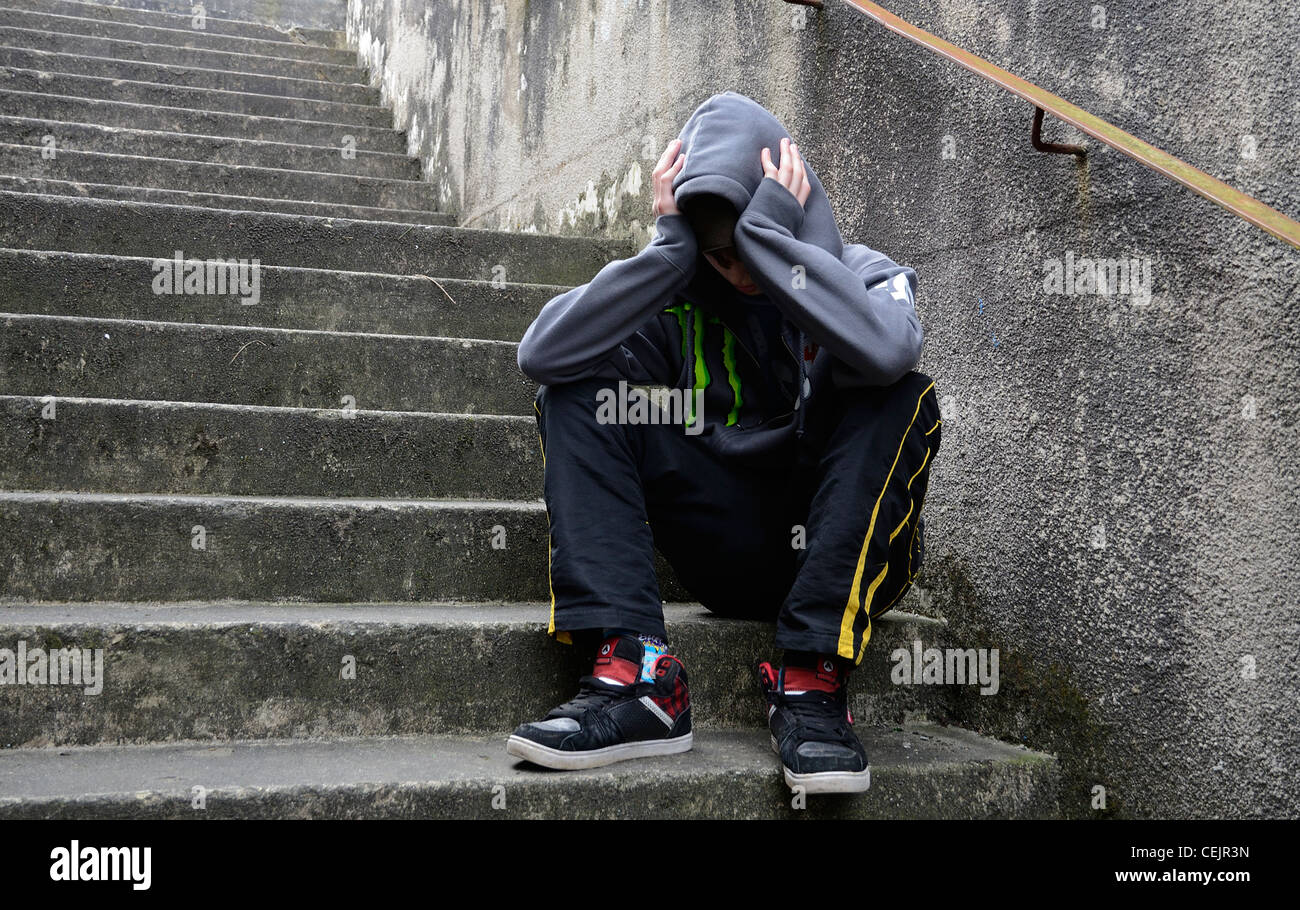 A  teenage boy  sat with his head in hands on steps Stock Photo