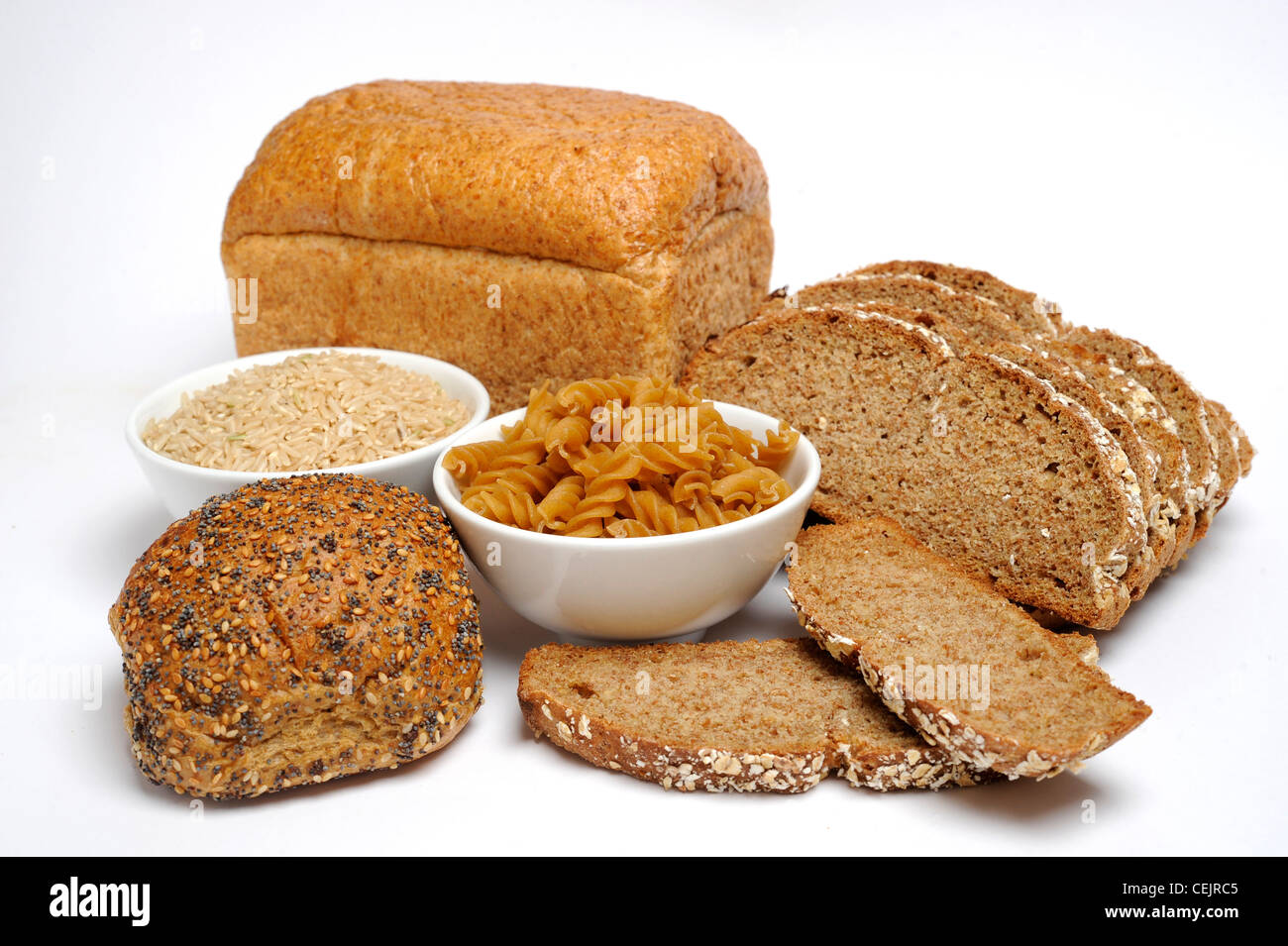 Two bowls filled with long grain rice and dried fusilli pasta surrounded by loaves of bread Stock Photo