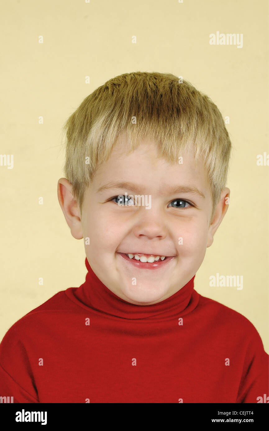 Blonde three year old boy wearing red turtle neck jumper smiling at the camera Baba and Kleuter Stock Photo