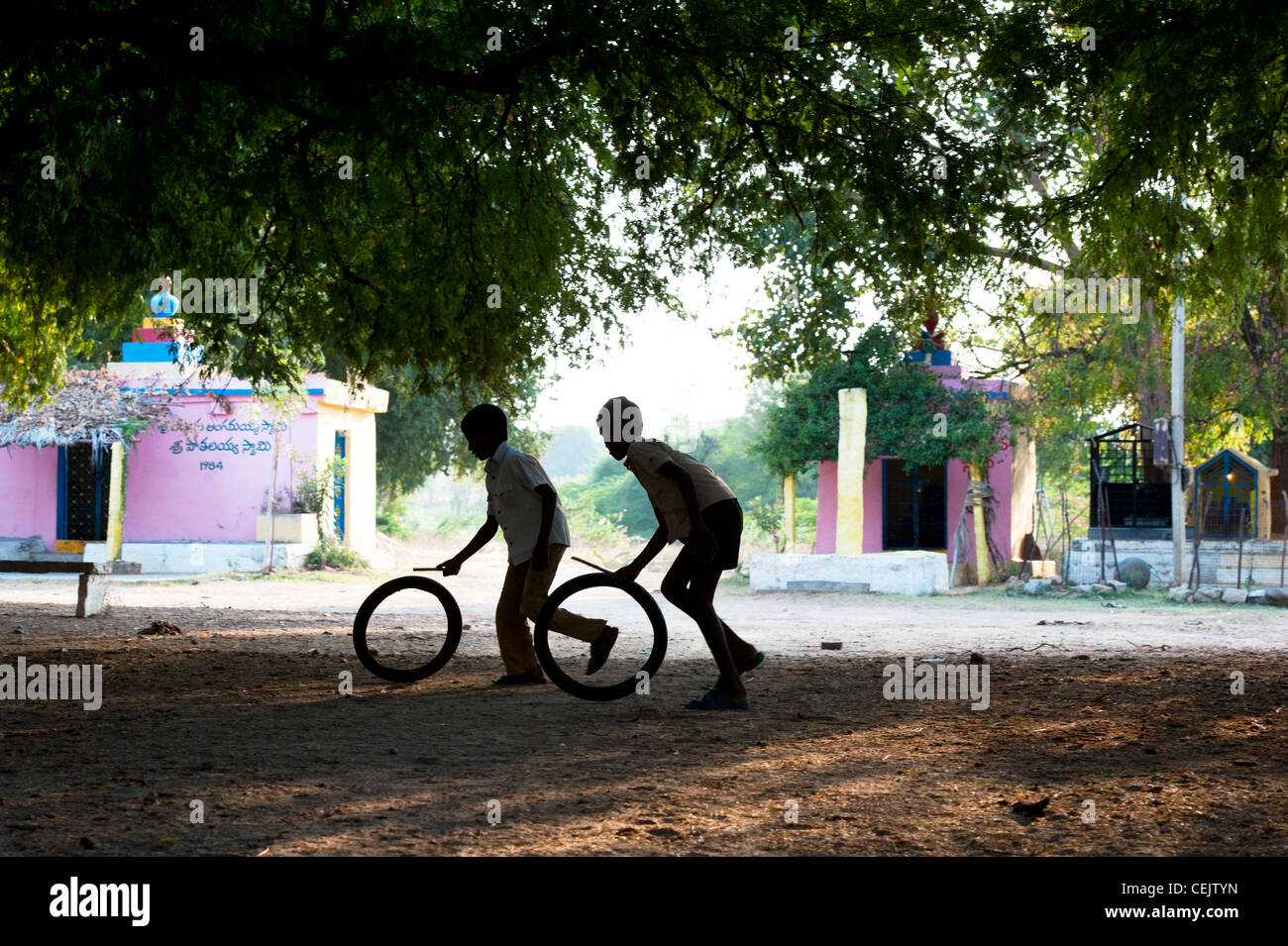 Indian boys playing with tyres under trees in the indian countryside. Silhouette. Andhra Pradesh, India Stock Photo