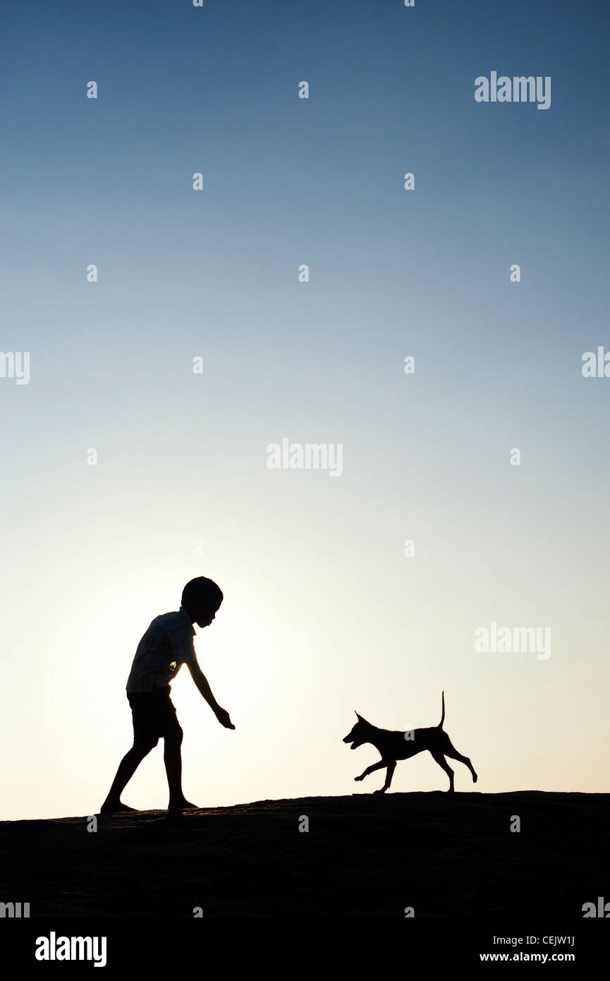 Silhouette of young Indian boy playing with his puppy. India Stock Photo
