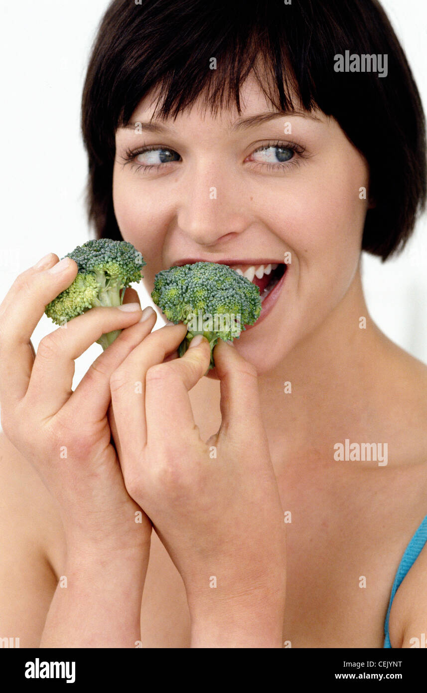 A  Female looking to the right eating raw broccoli Stock Photo
