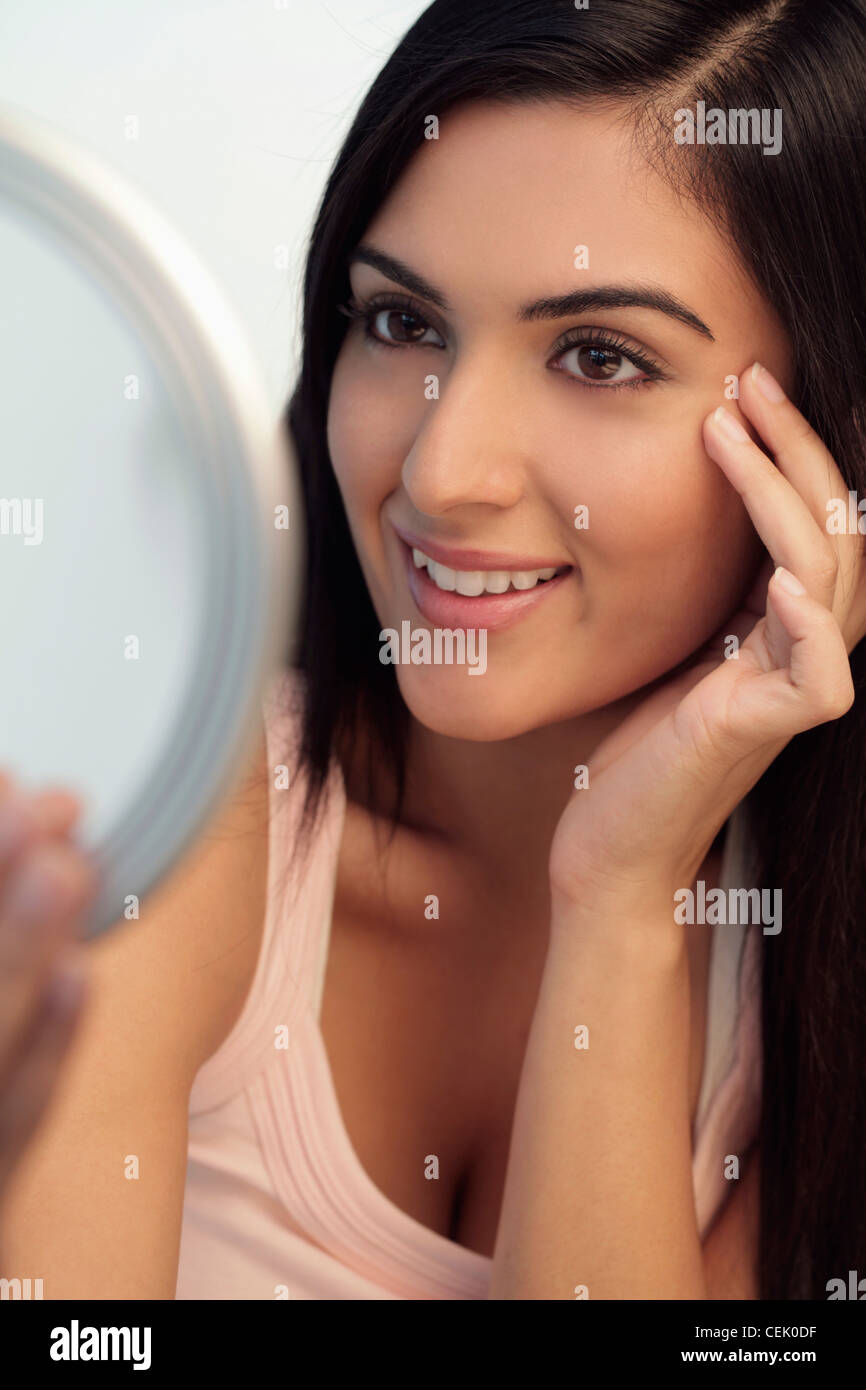 Young woman looking at mirror smiling while touching her face Stock
