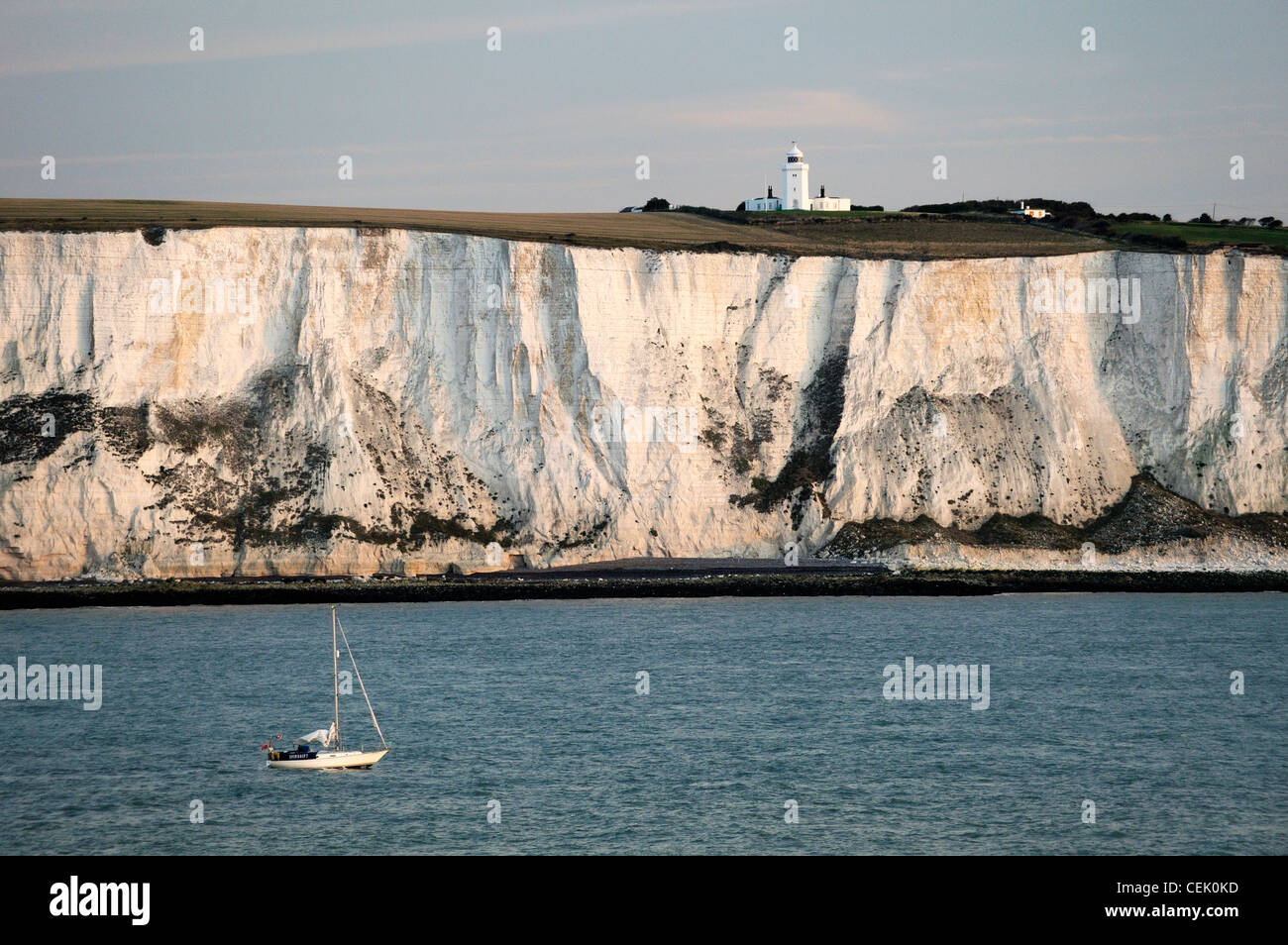 Yacht passing along the White cliffs of Dover in the English Channel east of Dover below South Foreland lighthouse. Dawn light Stock Photo