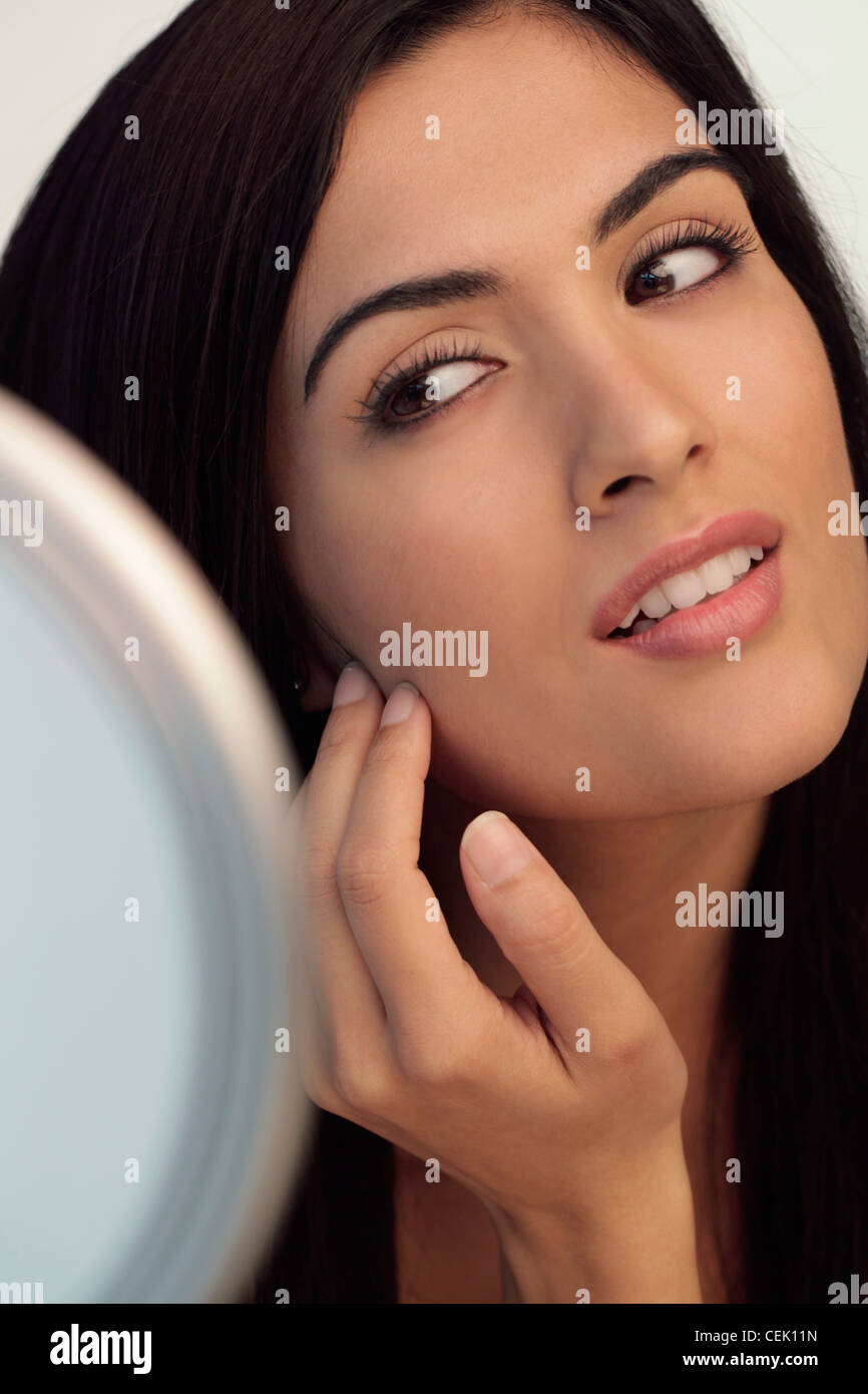 Young woman touching her face while looking at mirror Stock Photo - Alamy