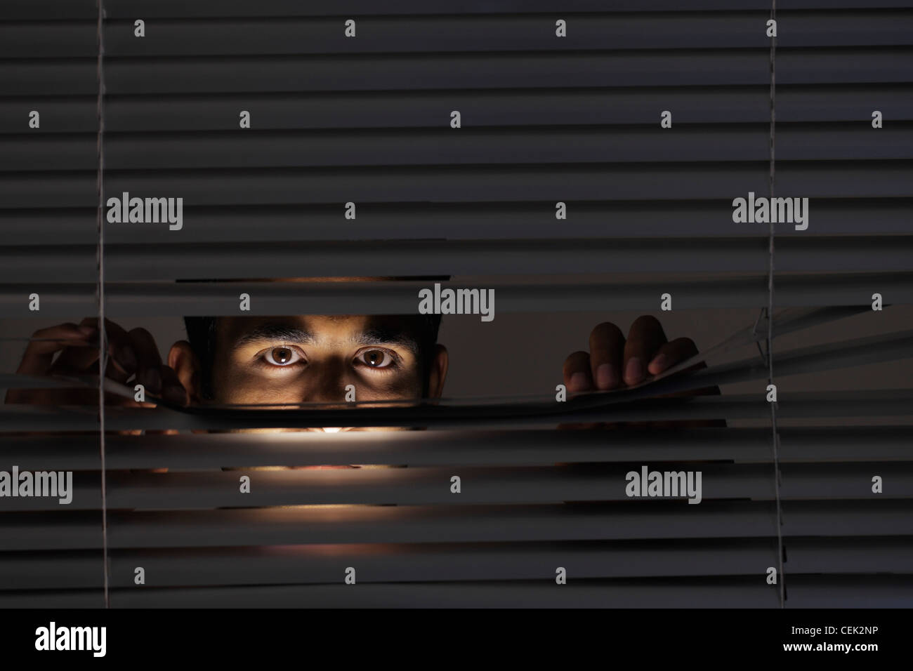Young man looking through blinds with just his eyes visible Stock Photo