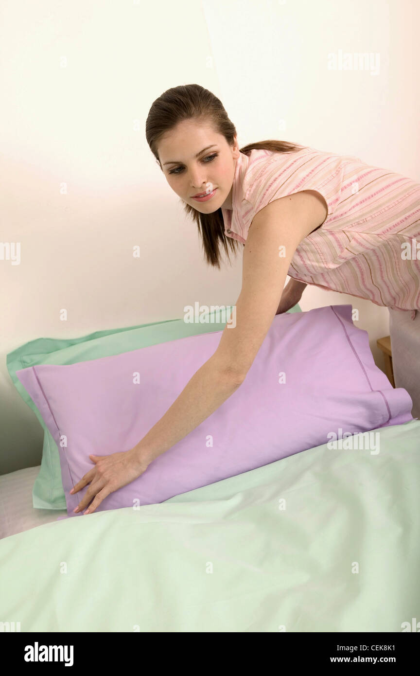 Female brunette hair off face wearing sleeveless pink and green striped shirt and cream linen skirt leaning over bed Stock Photo