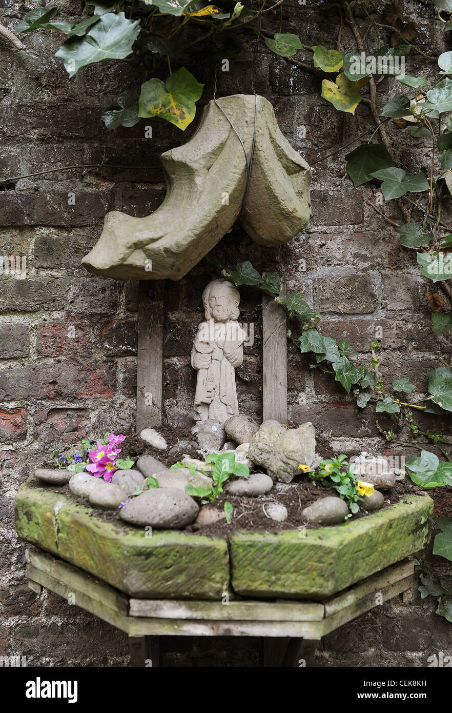 Hidden Treasure Garden feature on the wall with pebbles and saint sculpture Stock Photo