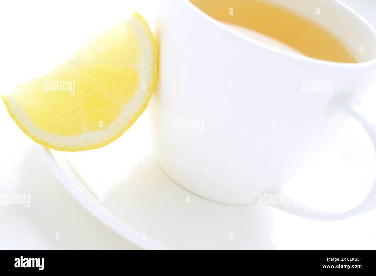 A close up of a white cup and saucer filled with a yellow fruit tea, with a slice of lemon on one side Stock Photo