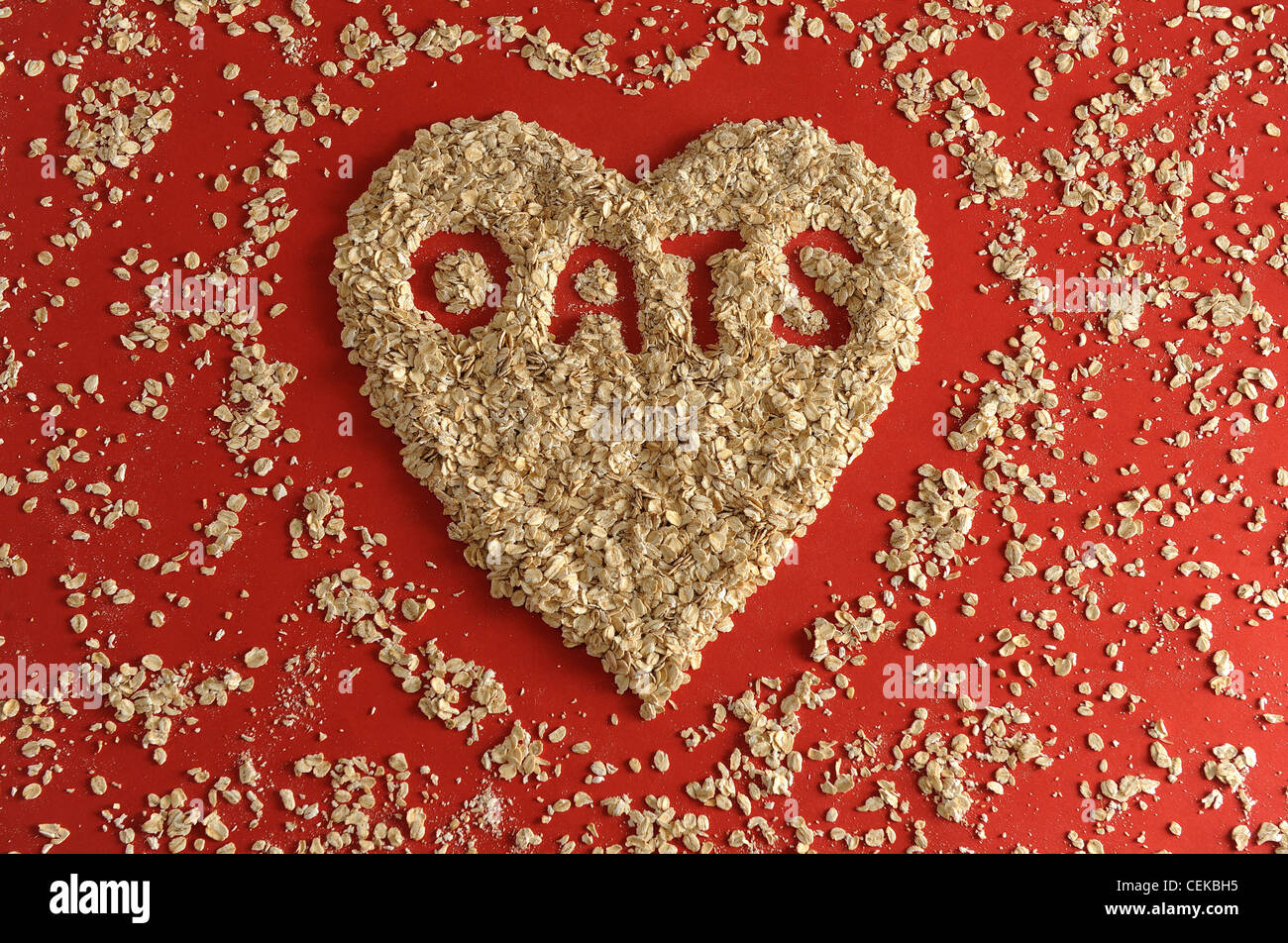 A still life image of dry porridge oats in heart shape on red background and the word Oats spelt inside it Stock Photo