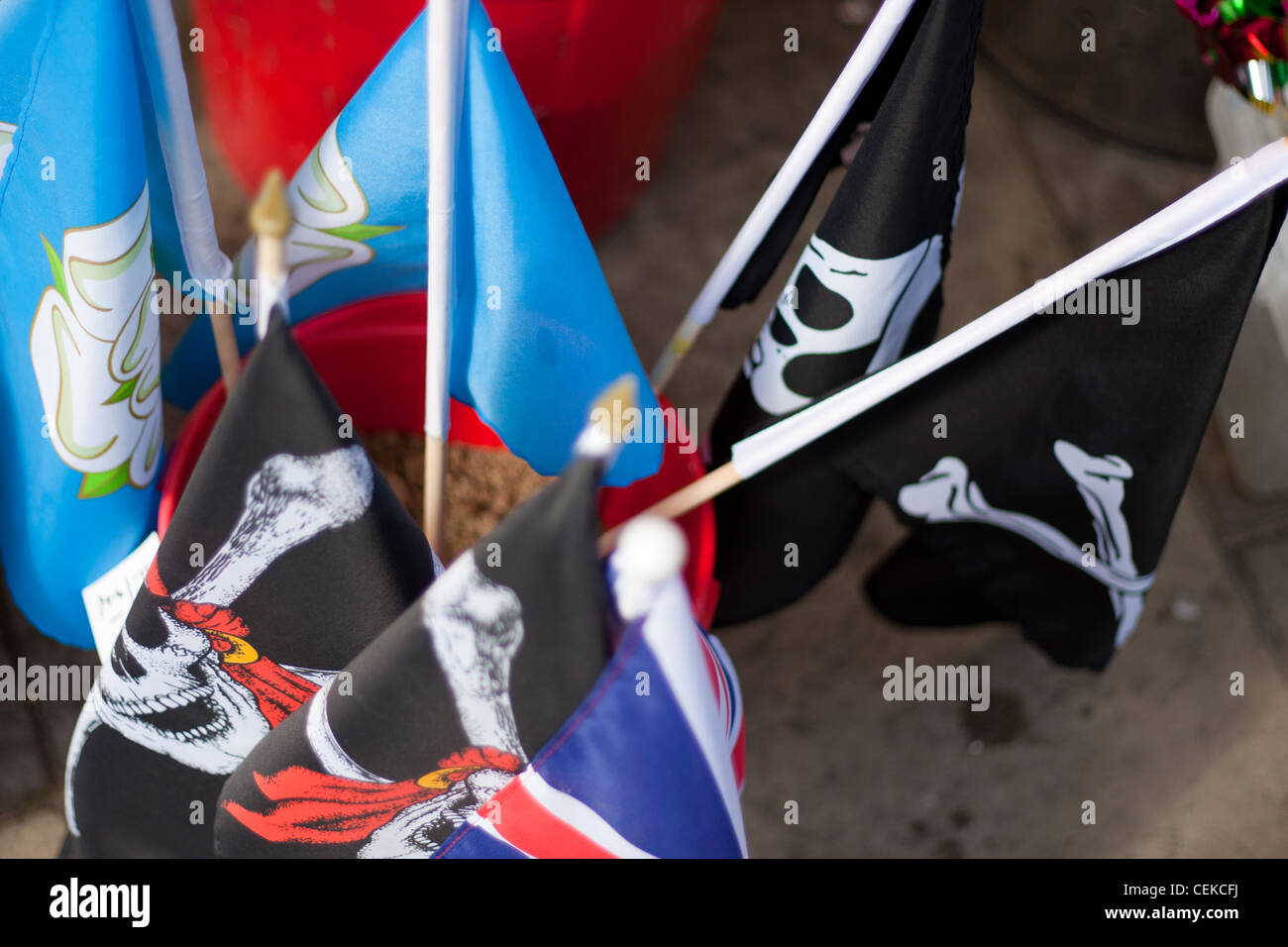 A bucket of sand holding many flags including pirate skull and crossbones flags ready to buy by tourists at the seaside Stock Photo