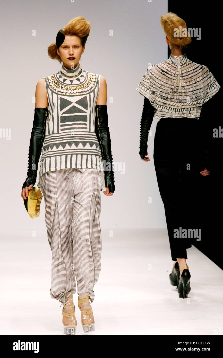 Patterned sleeveles top, fingerless long black gloves zips, patterned baggy trousers, cleat platform shoes and gold handbag Stock Photo