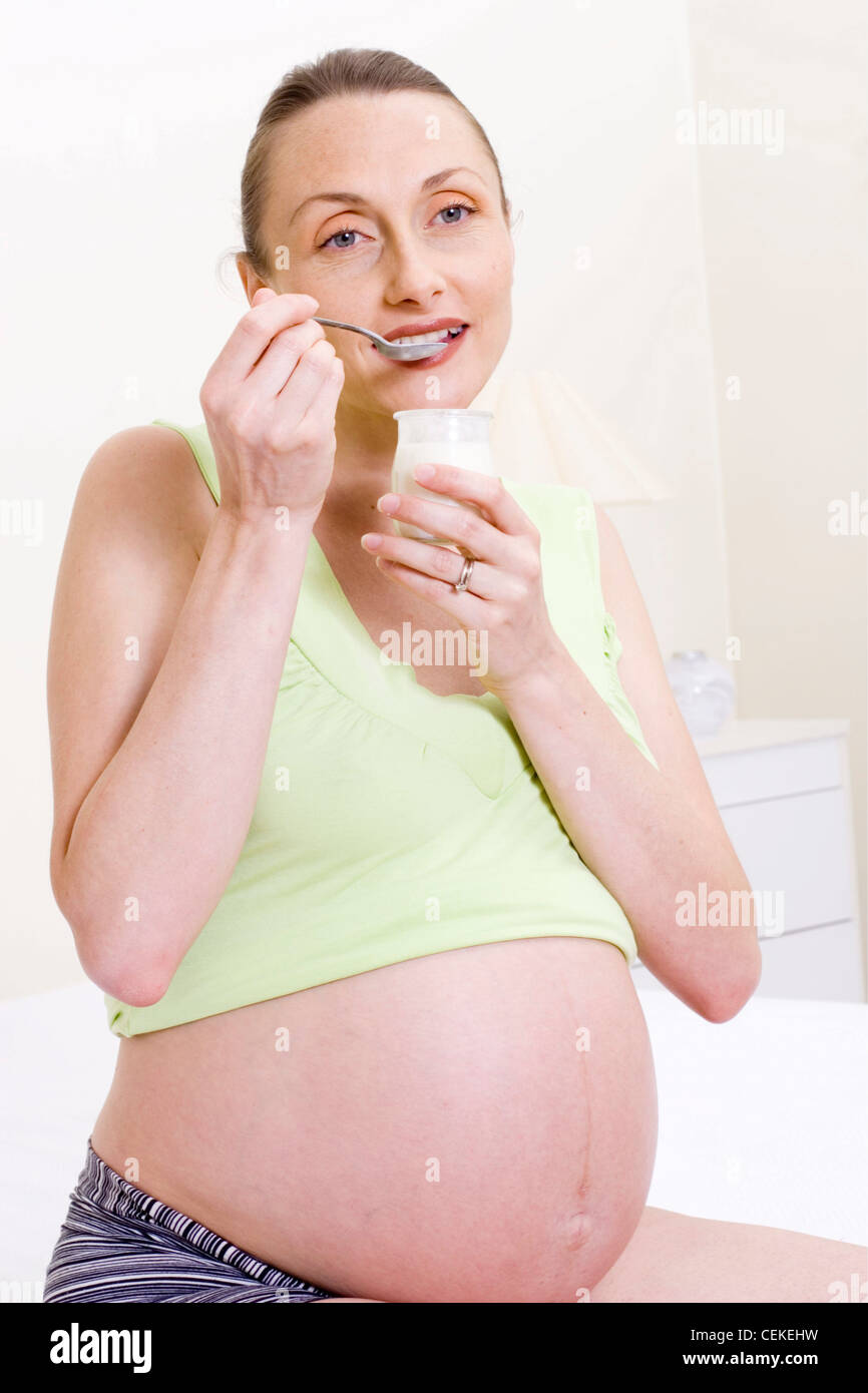 Female blonde ponytail hair, wearing striped blue bottoms and strappy green top  pushed up to expose heavily pregnant stomach Stock Photo