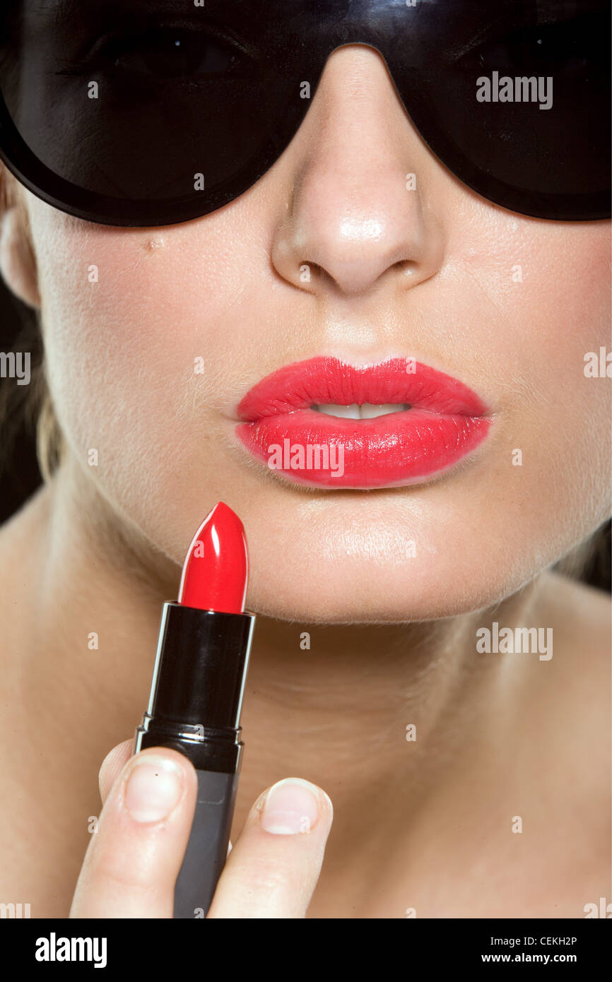 Female wearing bright red lipstick and large black sunglasses, holding