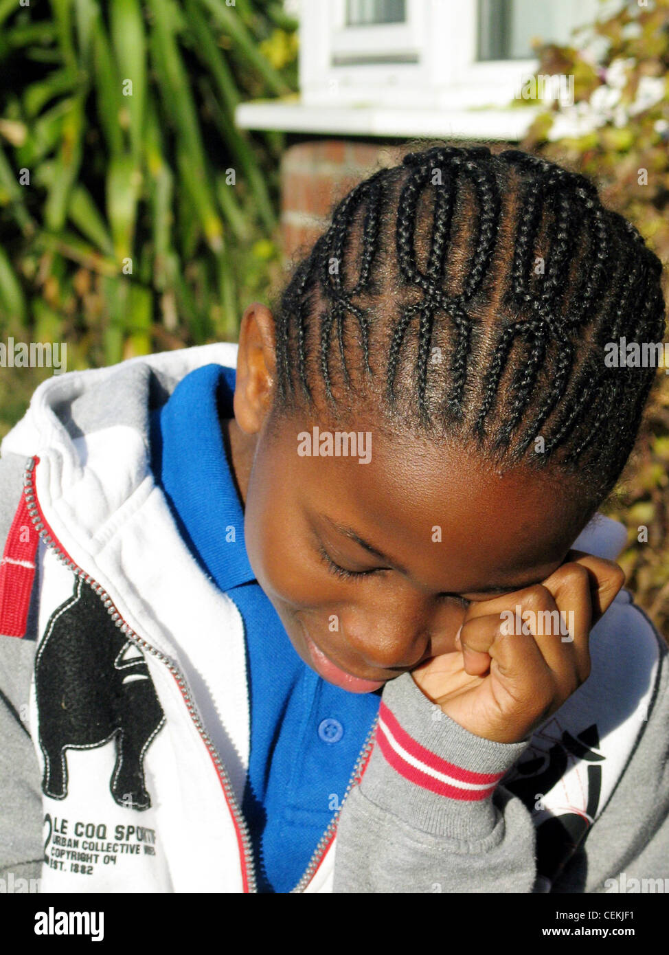 Male black child of years with cornrow braided hair, with head on hand and eyes closed Stock Photo