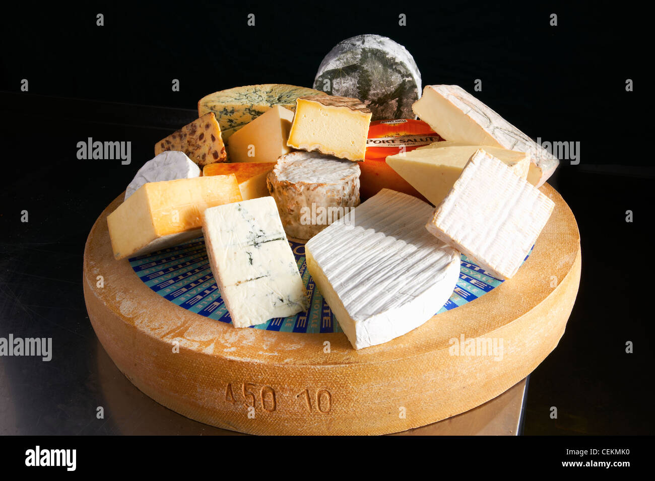 A Display of a range of cheeses set on one whole cheese and woodblock on a neutral, dark background. Stock Photo