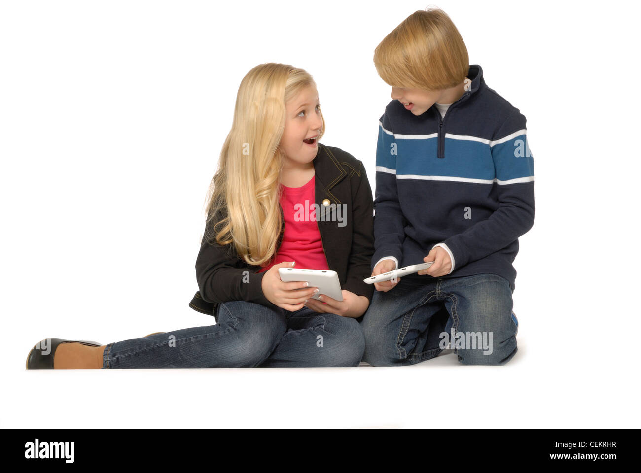 Ten year old girl and eleven year old boy using tablet computers or eBook readers and smiling. Stock Photo