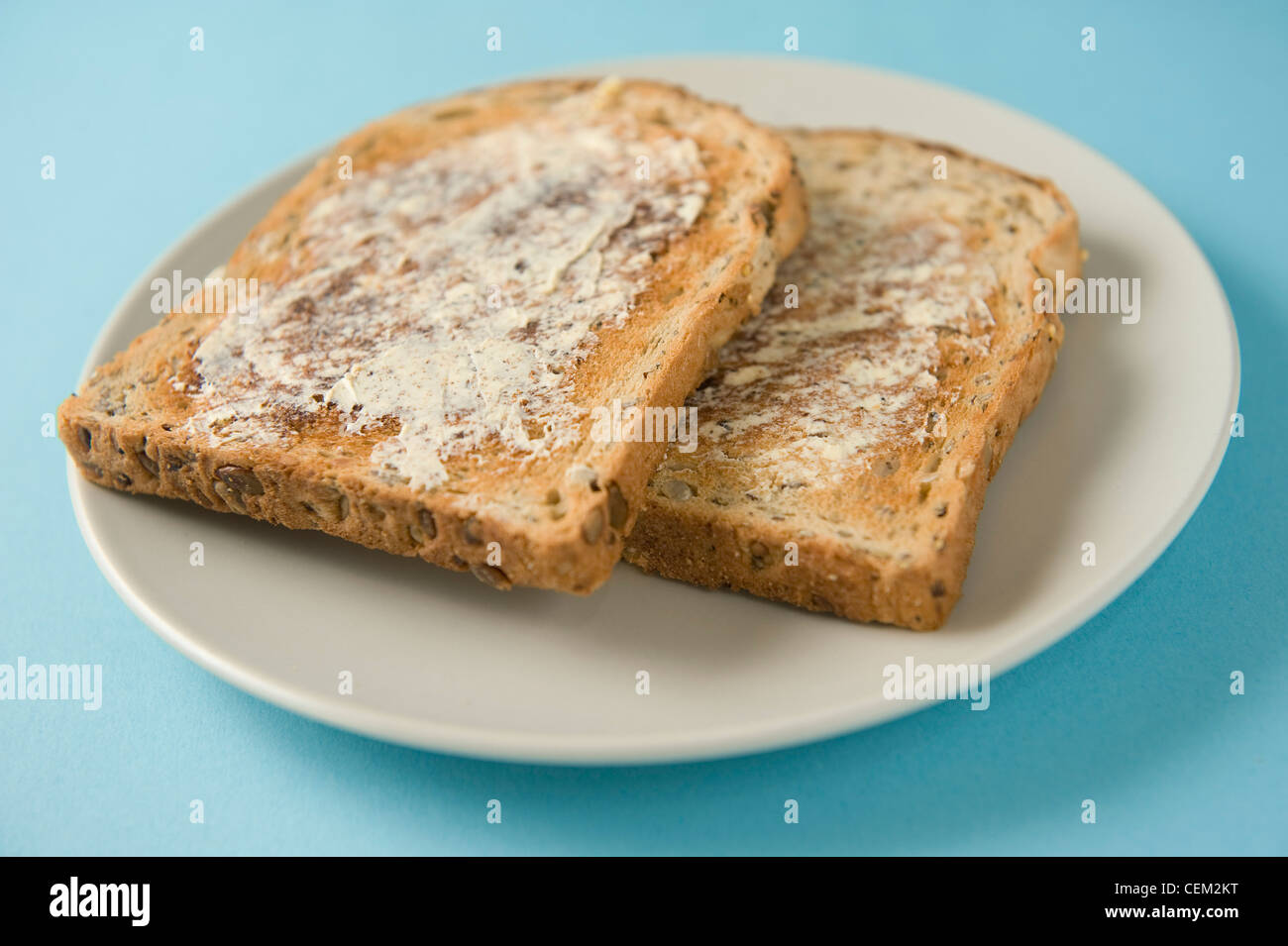 Two slices of toasted bread with sunflower seeds and butter on white