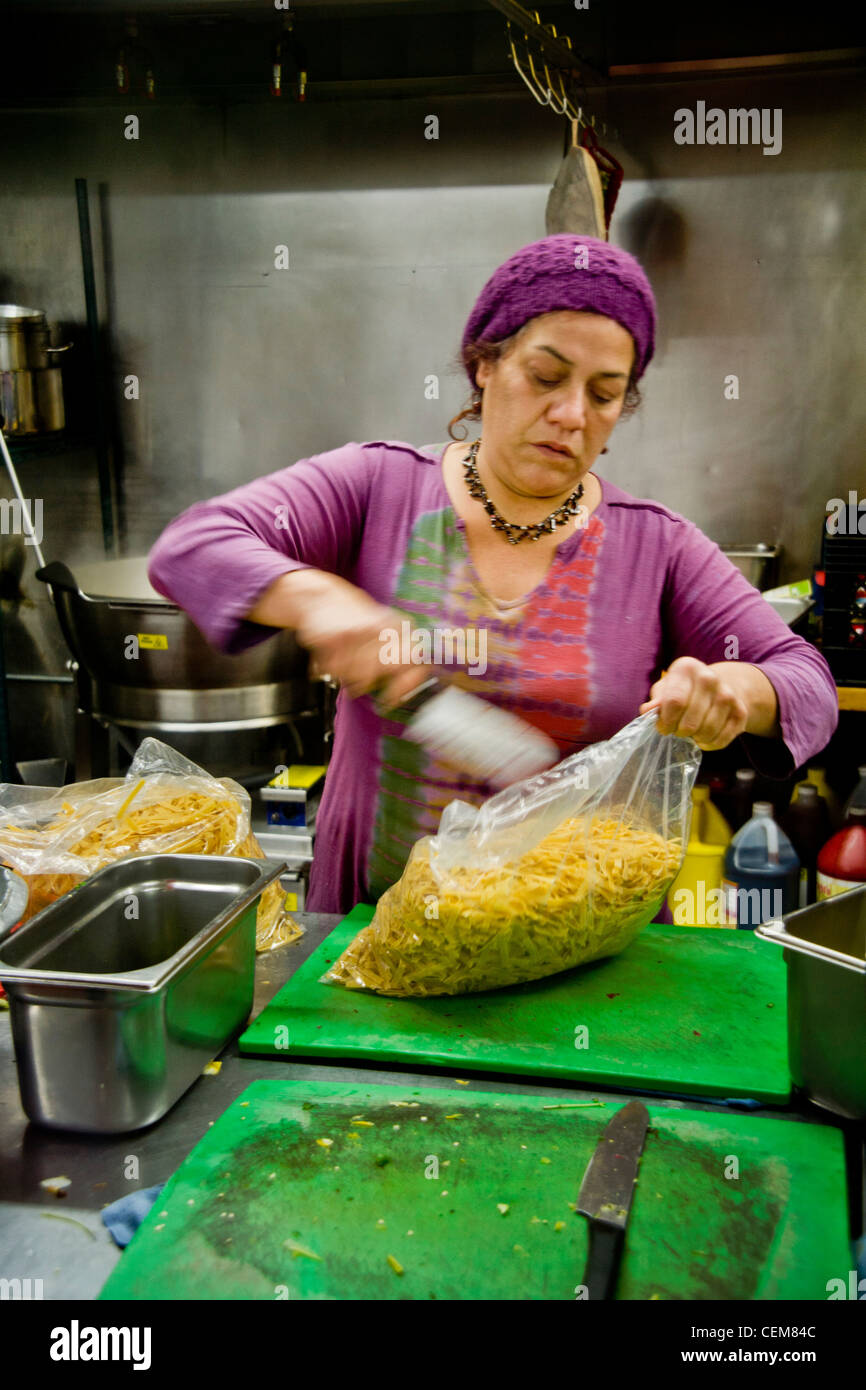 The Hispanic cook of a Costa Mesa, CA, soup kitchen to feed the homeless uses a knife to open a bag of pasta. Stock Photo